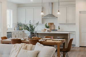 Kitchen with wall chimney exhaust hood, decorative light fixtures, dishwasher, light hardwood / wood-style floors, and decorative backsplash