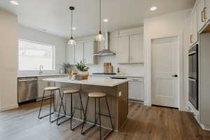 Kitchen with white cabinetry, stainless steel dishwasher, a kitchen island, wall chimney range hood, and backsplash