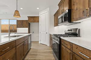 Kitchen featuring light stone countertops, pendant lighting, stainless steel appliances, and sink