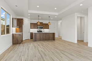 Kitchen featuring range, decorative light fixtures, light hardwood / wood-style flooring, and a kitchen island with sink