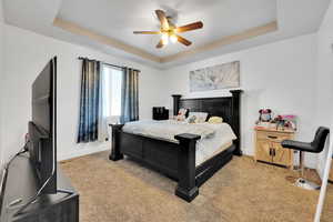 Bedroom featuring a tray ceiling, ceiling fan, and light carpet