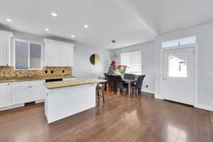 Kitchen with light stone countertops, sink, decorative light fixtures, a center island, and white cabinetry