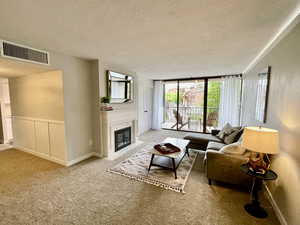 Carpeted living room with a fireplace, a textured ceiling, and a wall of windows