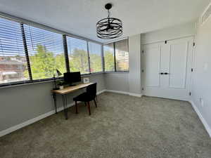 Carpeted office space with a textured ceiling and a chandelier