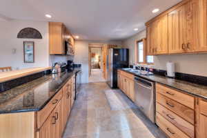 Kitchen with dark stone countertops, sink, stainless steel appliances, and light brown cabinets