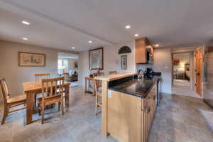 Kitchen featuring kitchen peninsula, appliances with stainless steel finishes, light brown cabinetry, beam ceiling, and a breakfast bar area