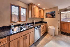 Kitchen featuring stainless steel dishwasher, dark stone counters, and sink