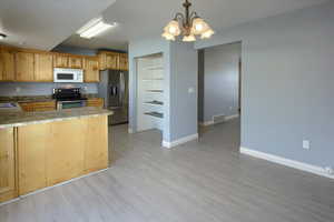 Kitchen with pendant lighting, light hardwood / wood-style flooring, stainless steel appliances, and an inviting chandelier