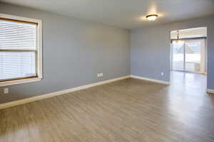 Spare room with a wealth of natural light, wood-type flooring, and an inviting chandelier