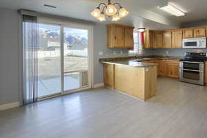 Kitchen featuring hanging light fixtures, an inviting chandelier, light hardwood / wood-style flooring, kitchen peninsula, and stainless steel electric range