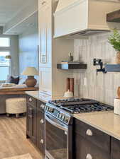 Kitchen featuring gas stove, dark brown cabinetry, tasteful backsplash, light hardwood / wood-style flooring, and premium range hood