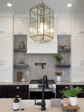 Kitchen with white cabinets, decorative light fixtures, tasteful backsplash, and stainless steel range with gas stovetop