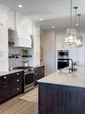 Kitchen with white cabinets, hanging light fixtures, appliances with stainless steel finishes, and light hardwood / wood-style flooring