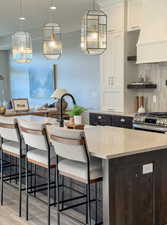 Kitchen featuring exhaust hood, decorative backsplash, light wood-type flooring, a kitchen island, and white cabinetry