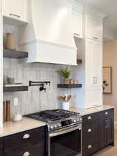 Kitchen with tasteful backsplash, dark brown cabinetry, white cabinets, and stainless steel gas range