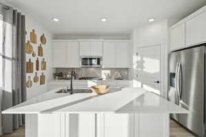 Kitchen featuring white cabinetry, a kitchen island with sink, sink, and appliances with stainless steel finishes