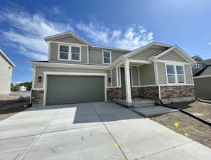 Craftsman-style house with stone siding, an attached garage, driveway, and a porch