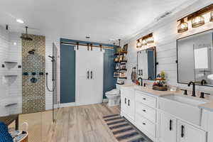 Bathroom with a tile shower, vanity, a textured ceiling, toilet, and wood walls