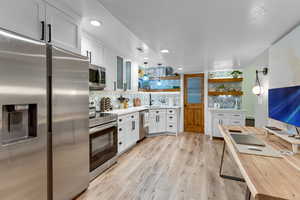 Kitchen with tasteful backsplash, white cabinetry, hanging light fixtures, and stainless steel appliances