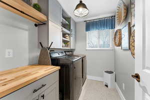 Clothes washing area with cabinets, washer and dryer, and light tile patterned flooring