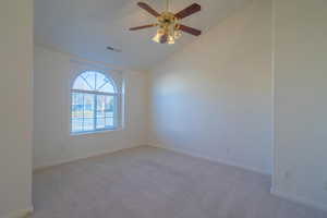 Carpeted spare room with ceiling fan and vaulted ceiling