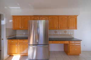 Kitchen with backsplash, stainless steel refrigerator, ornamental molding, and light tile patterned flooring