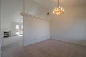 Empty room with a chandelier, a tiled fireplace, light carpet, and vaulted ceiling