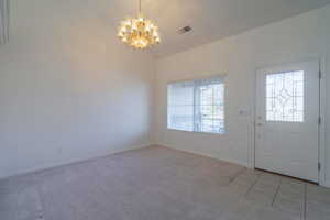 Carpeted foyer entrance with vaulted ceiling and an inviting chandelier