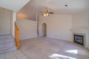 Unfurnished living room featuring light colored carpet, ceiling fan, lofted ceiling, and a tiled fireplace