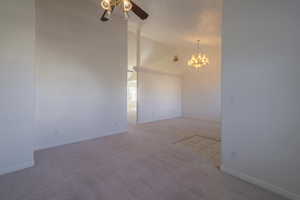 Spare room featuring ceiling fan with notable chandelier, lofted ceiling, and light carpet