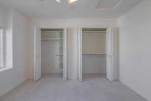 Unfurnished bedroom featuring ceiling fan, light colored carpet, and two closets