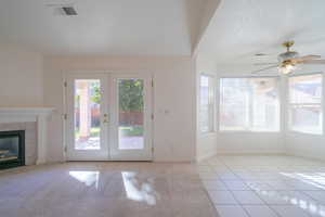 Unfurnished living room featuring a tile fireplace, ceiling fan, french doors, and light tile patterned floors