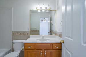 Bathroom featuring ceiling fan, toilet, a bathtub, vanity, and tile walls