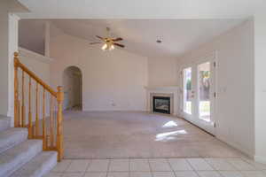 Unfurnished living room featuring lofted ceiling, french doors, ceiling fan, light tile patterned flooring, and a tiled fireplace