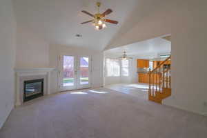 Unfurnished living room with ceiling fan, a fireplace, light colored carpet, and french doors