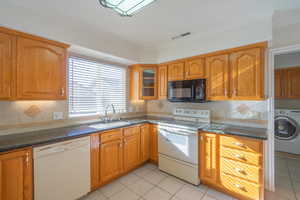 Kitchen featuring ornamental molding, white appliances, dark stone countertops, washer / clothes dryer, and light tile patterned flooring