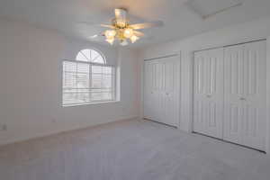 Unfurnished bedroom with ceiling fan, light carpet, and two closets