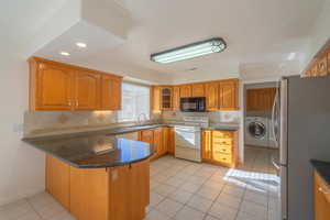 Kitchen featuring sink, light tile patterned floors, white range with electric stovetop, kitchen peninsula, and stainless steel refrigerator