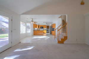 Unfurnished living room featuring light carpet, ceiling fan, and vaulted ceiling