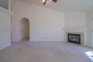 Unfurnished living room featuring ceiling fan, a fireplace, light carpet, and lofted ceiling