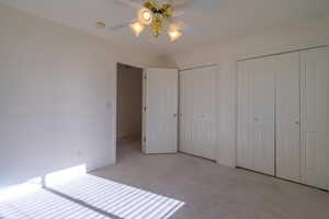 Unfurnished bedroom with ceiling fan, light carpet, and multiple closets