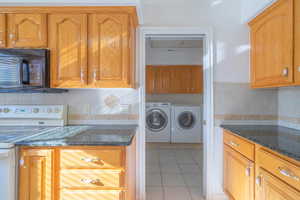 Kitchen featuring tasteful backsplash, washer and clothes dryer, dark stone countertops, white electric range, and light tile patterned flooring