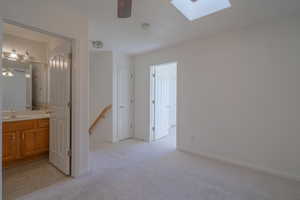 Interior space featuring connected bathroom, a skylight, sink, and light colored carpet