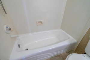 Bathroom with tile patterned flooring, toilet, and a tub to relax in