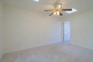 Carpeted empty room featuring a skylight and ceiling fan