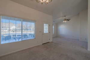 Carpeted entryway with ceiling fan with notable chandelier and vaulted ceiling