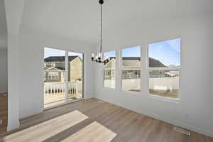 Unfurnished dining area with hardwood / wood-style flooring, vaulted ceiling, and an inviting chandelier