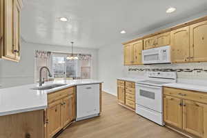 Kitchen with white appliances, sink, hanging light fixtures, light hardwood / wood-style flooring, and a chandelier