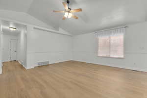 Empty room with ceiling fan, vaulted ceiling, and light wood-type flooring