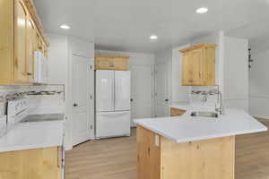 Kitchen featuring kitchen peninsula, decorative backsplash, white appliances, sink, and light brown cabinets